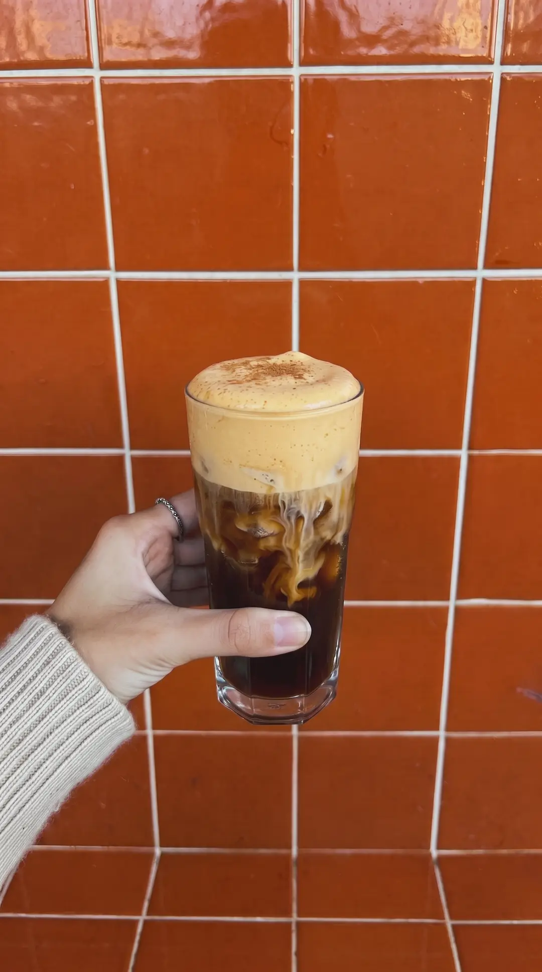 Cold brew con espuma de calabaza frente a una pared de azulejo terracota